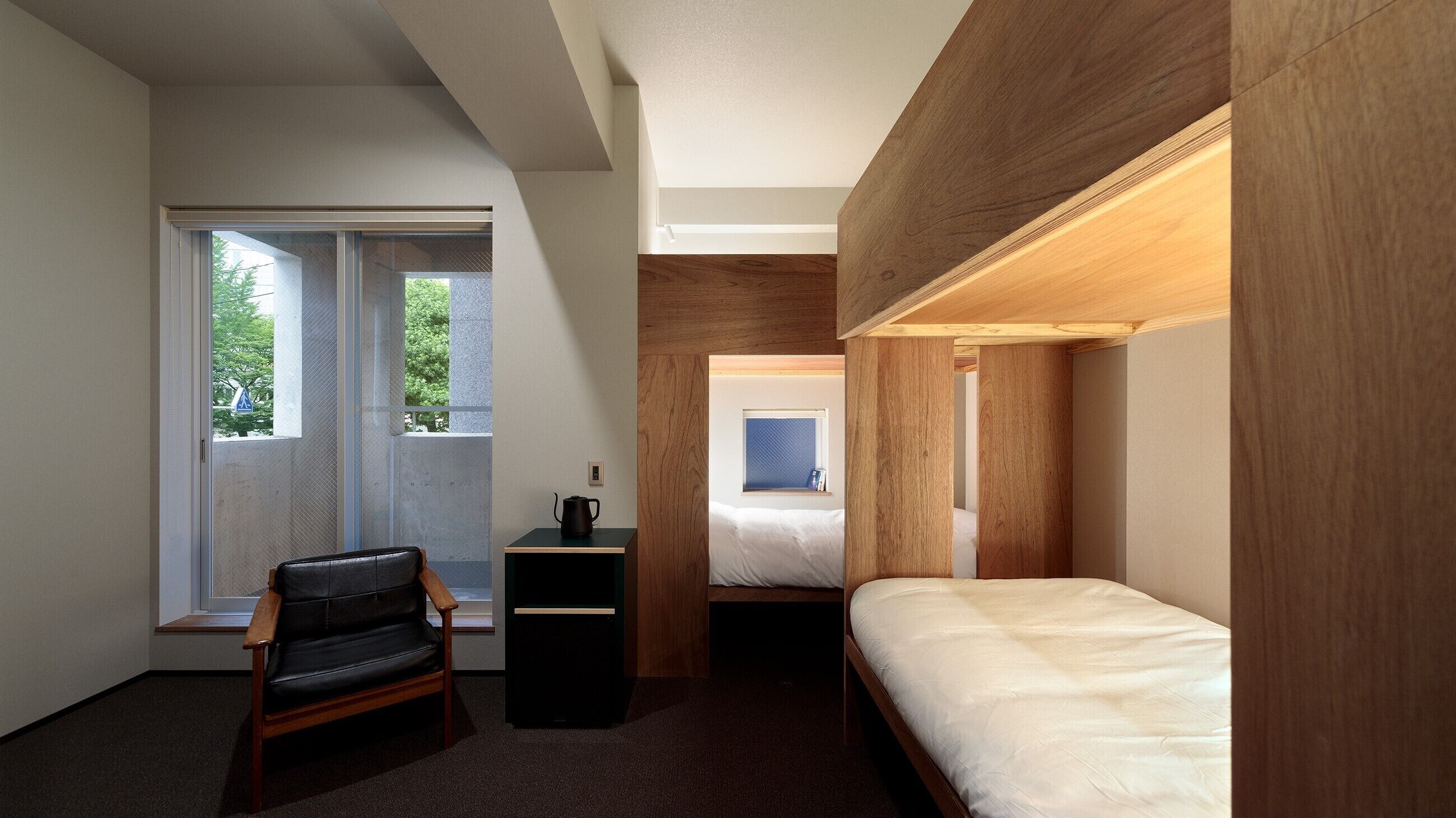 A compact hotel room with a bed, a desk, a chair, and a window with a view of trees.