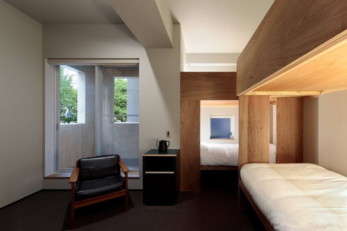 A compact hotel room with a bed, a desk, a chair, and a window with a view of trees.