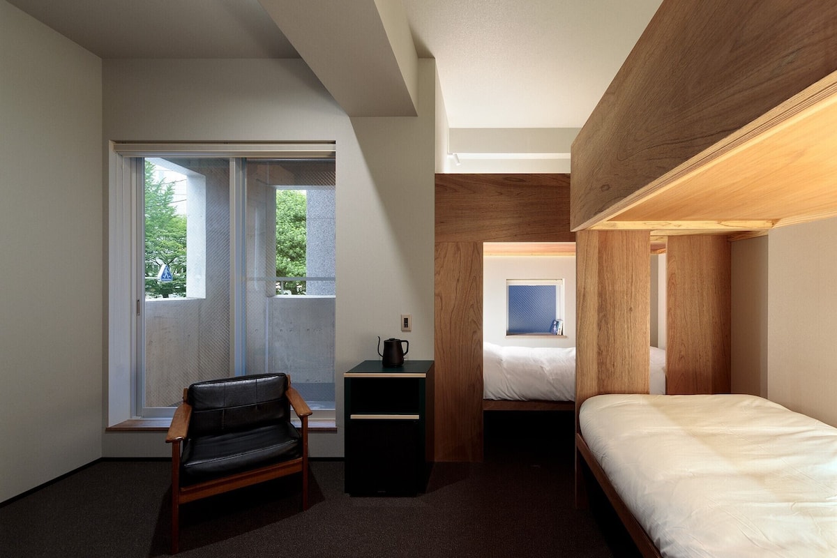A compact hotel room with a bed, a desk, a chair, and a window with a view of trees.