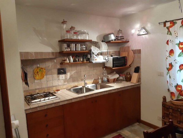 A compact kitchen with a gas stove, a sink, and various kitchen items on shelves. - Small cabin in a hamlet (Cuneo)