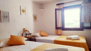 A hotel room with two single beds, a small table with a chair, and a window with curtains.