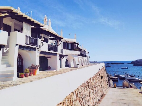 A coastal building with multiple balconies, a stone retaining wall, and a view of the sea with boats. - Fantastic house on the seafront in Binibeca (Binibequer)