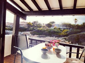 A balcony with a table set for two, overlooking a rocky landscape with vegetation and buildings in the distance. - Fantastic house on the seafront in Binibeca (Binibequer)