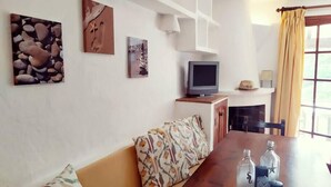 A living room with a sofa, a wooden coffee table, and a television on a stand. There are wall-mounted shelves above the sofa and a fireplace below.