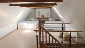 A loft bedroom with a sloped ceiling, a built-in bed, a wooden staircase, and a small table with decorative items. - Auvergne farmhouse in the heart of nature (CROS)