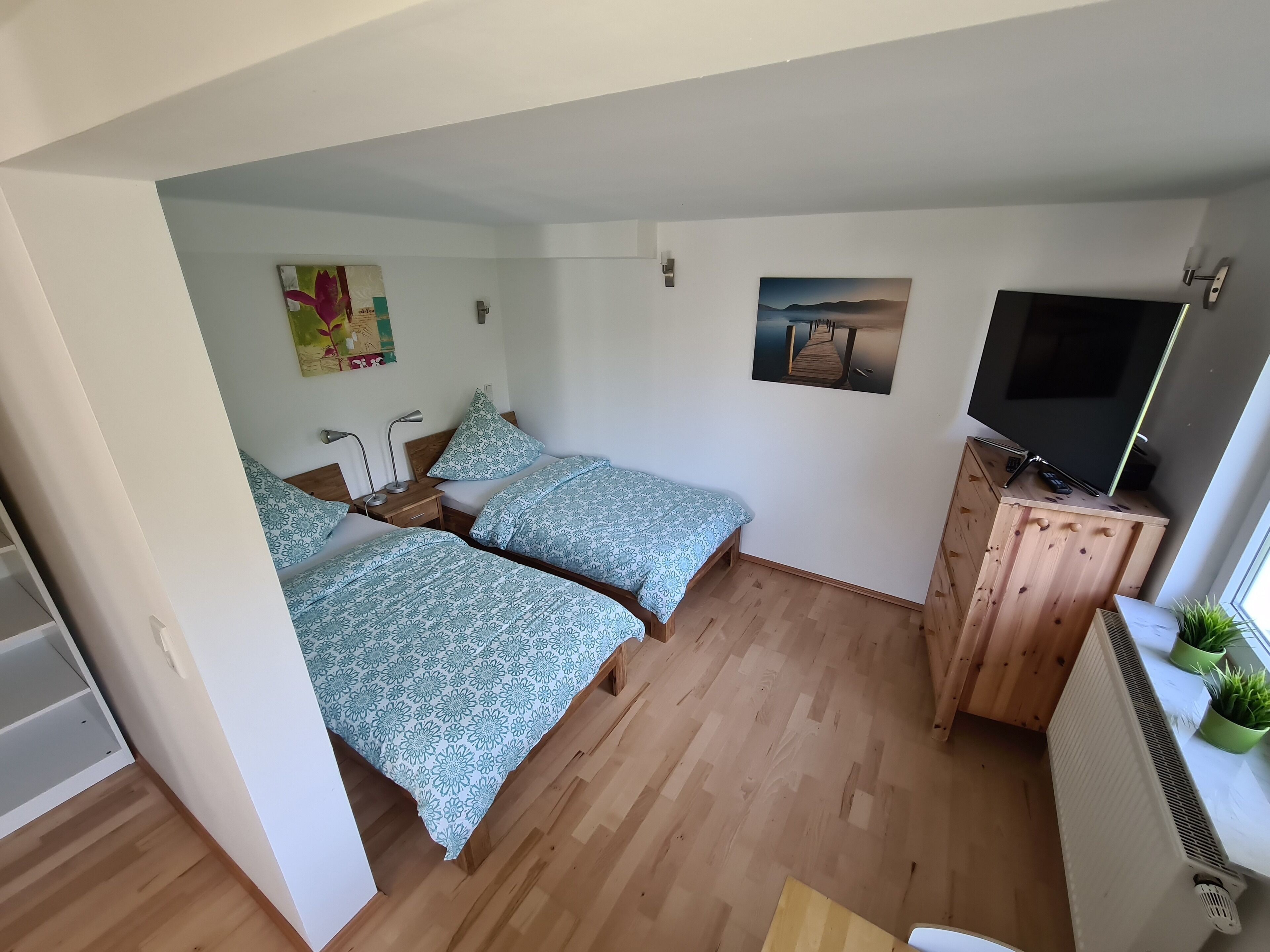 Una habitació petita i acollidora amb dos llits, un armari de fusta amb un televisor i un radiador.