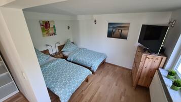 Una habitació petita i acollidora amb dos llits, un armari de fusta amb un televisor i un radiador.