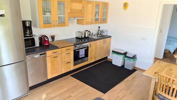A compact kitchen with wooden cabinets, a stainless steel refrigerator, a microwave, a toaster, and a sink.
