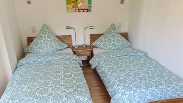 A room with two beds, each with a floral-patterned bedspread, a wooden headboard, a nightstand with a lamp, and a wall-mounted artwork.
