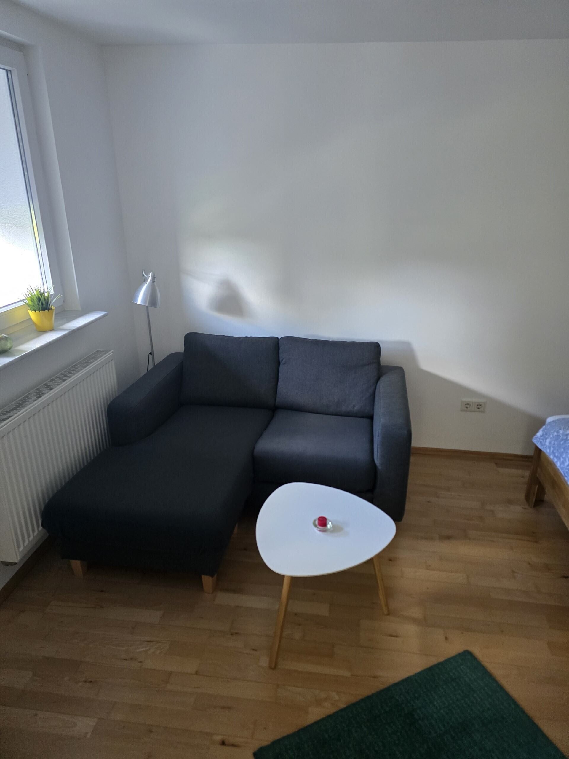 A modern living room with a sectional sofa, a small white table, a green rug, and a window with a plant.
