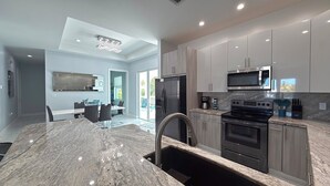 A modern kitchen with granite countertops, stainless steel appliances, and a dining area with a glass table and chairs. - Blue Paradise 5bed/5bath walking distance to the beach with a private pool (Marathon)
