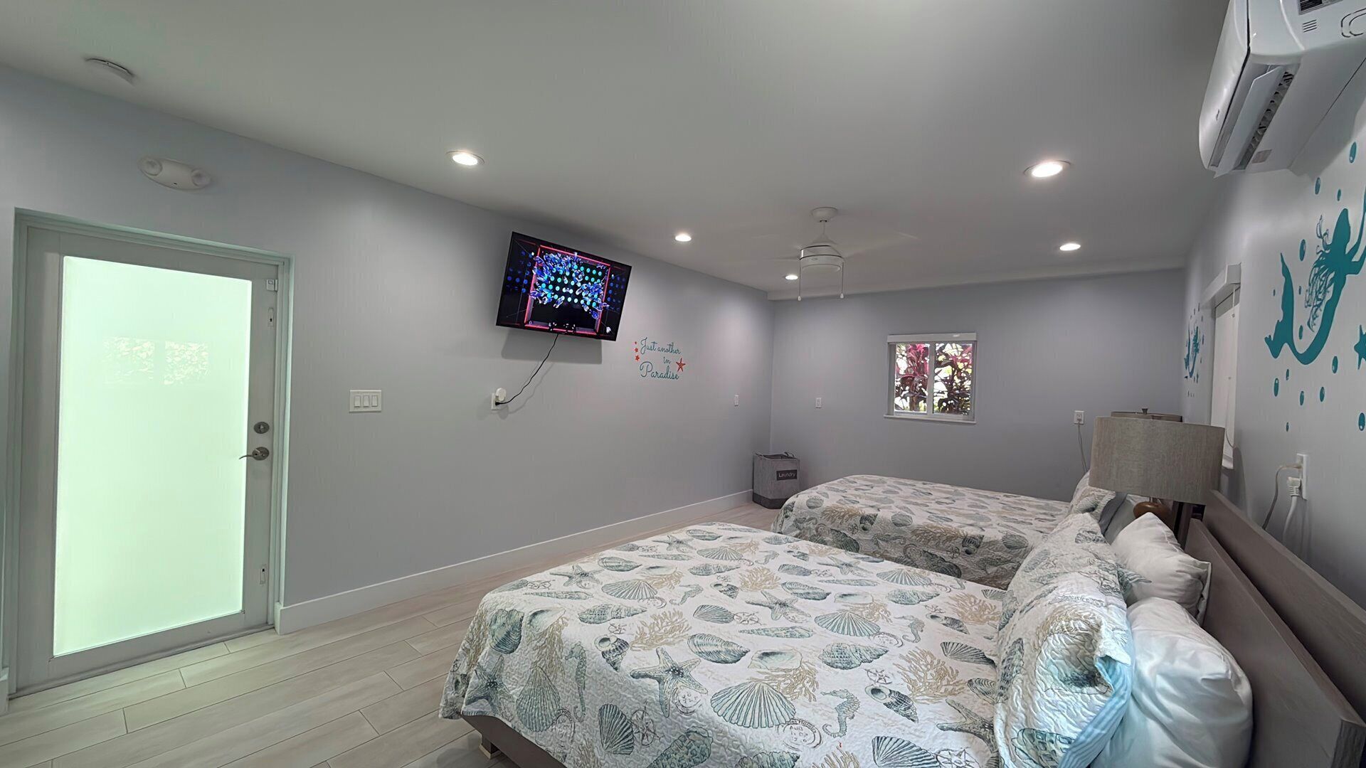 A bedroom with two beds, a television, a window, and a door.