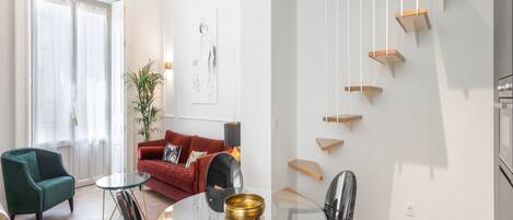 A modern living room with a glass dining table, red sofa, and a staircase with wooden steps.
