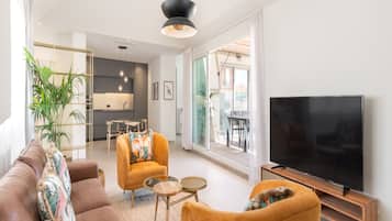 Een moderne woonkamer met een bank, fauteuils, een salontafel, een televisie en een eethoek op de achtergrond.
