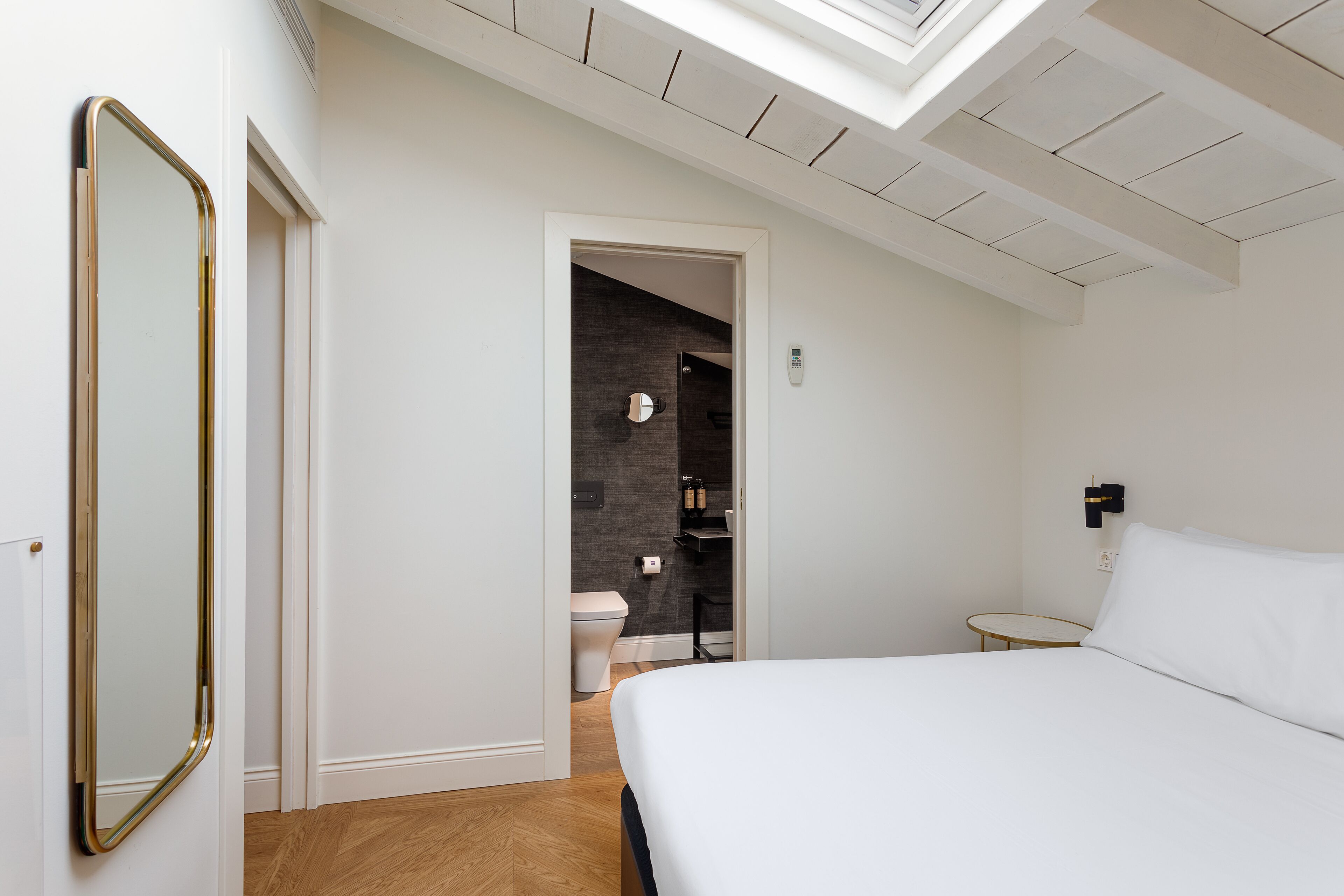 A bedroom with a bed, a bedside table, a mirror, and a view of the bathroom through an open door.