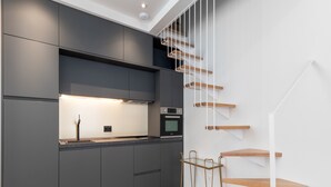 A modern kitchen with dark cabinetry, a built-in oven, and a wooden staircase with white railings. - Be Mate Málaga Centro (Málaga)