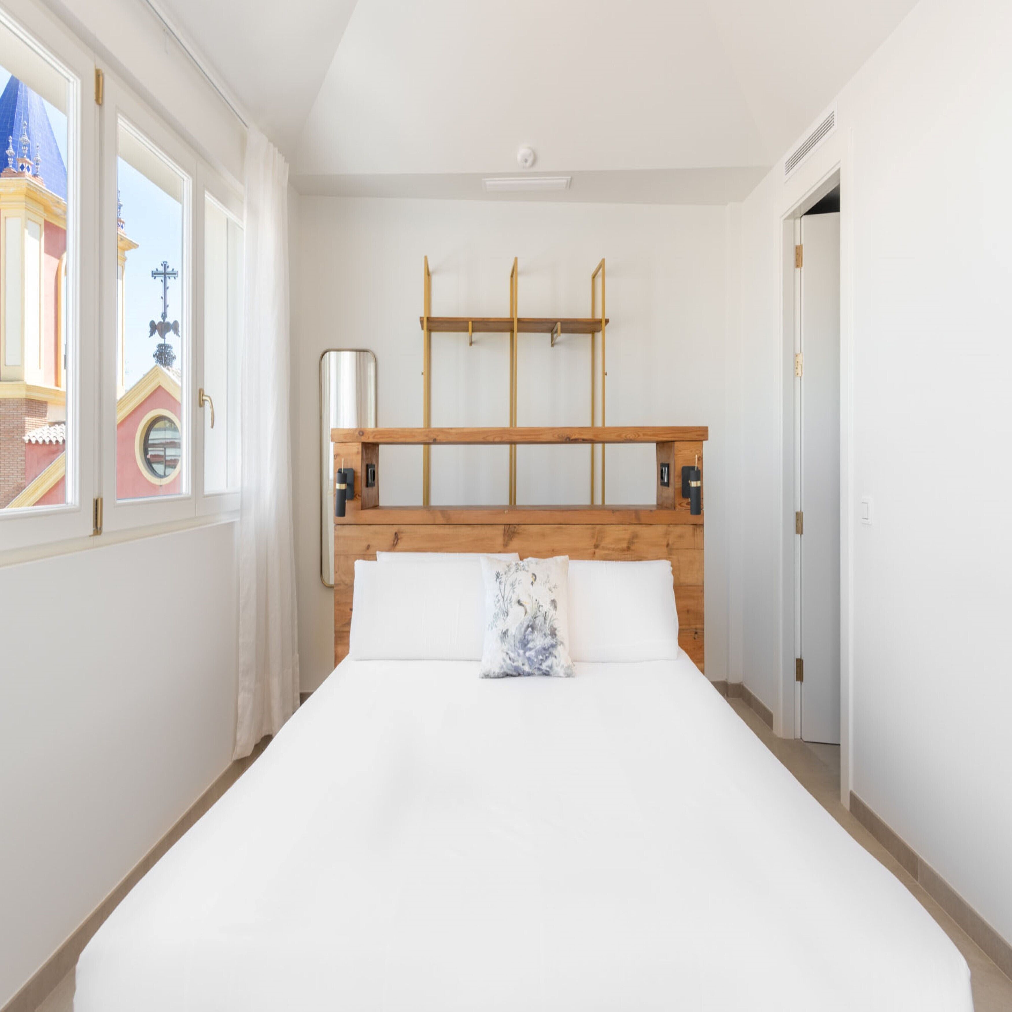 Ein Schlafzimmer mit einem Holz-Kopfteil, einem Bett mit weißer Bettwäsche und einem Fenster mit Blick auf ein Gebäude.