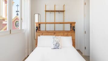 A bedroom with a wooden headboard, a bed with white bedding, and a window with a view of a building.