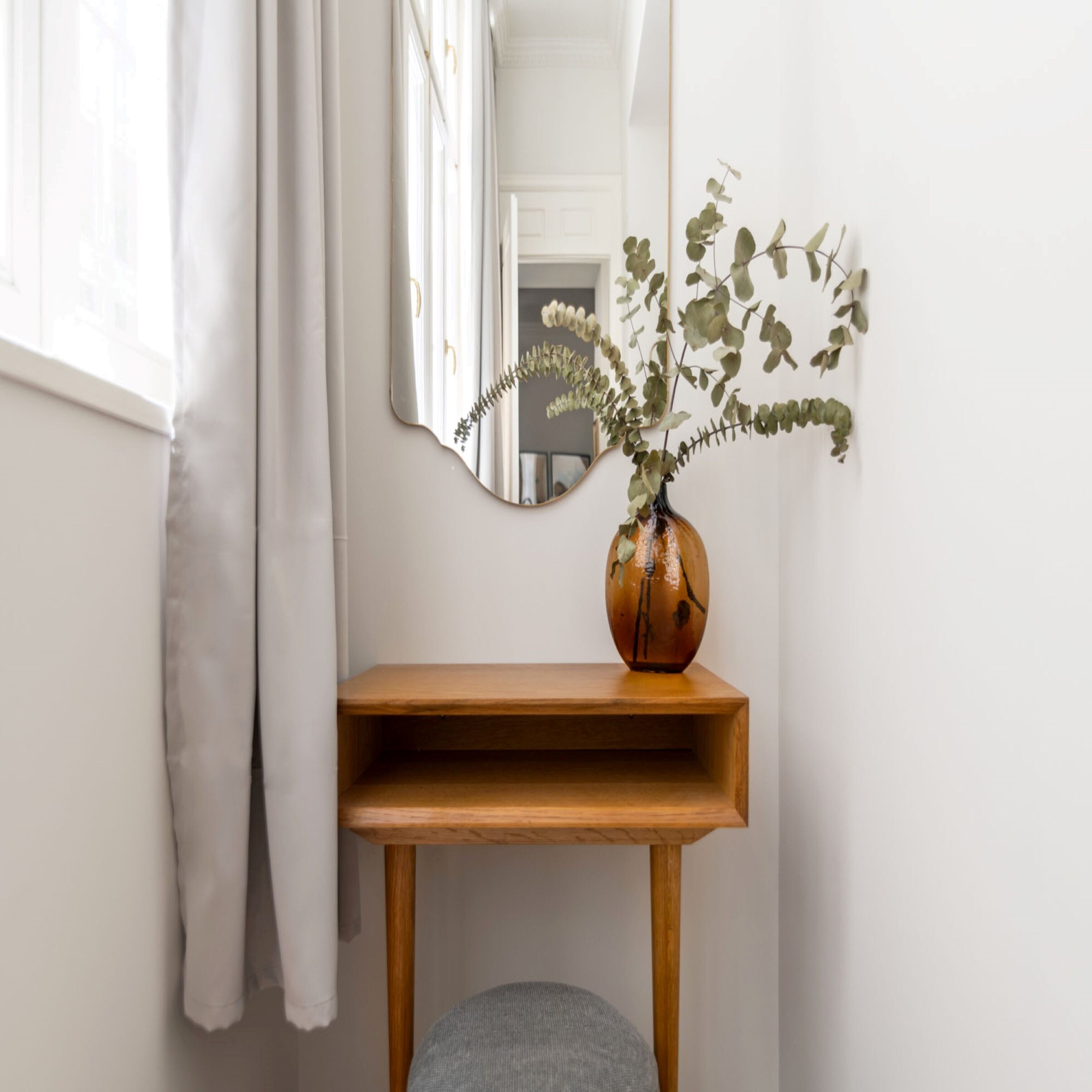 Un coin aménagé avec une console en bois, un vase rempli de feuillage vert et un miroir accroché au mur.