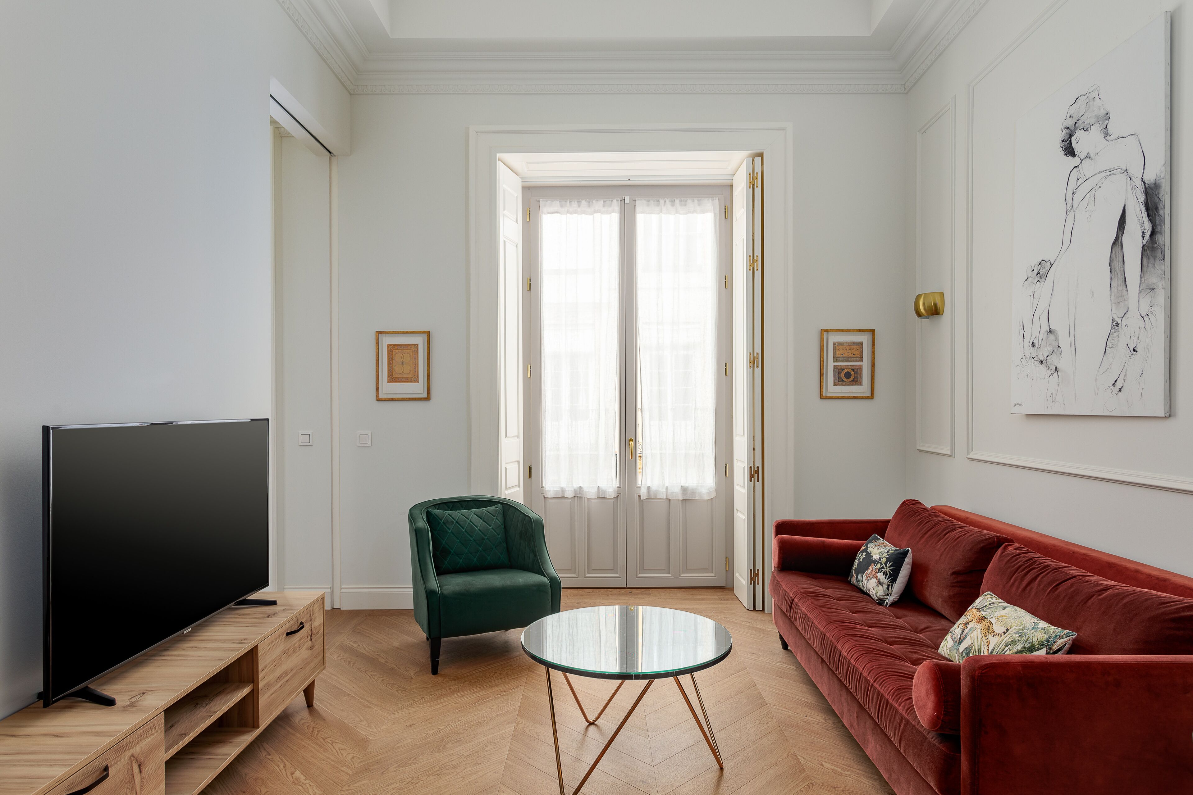 Ein Wohnzimmer mit Fernseher, einem grünen Sessel, einem roten Sofa und einem Glastisch.