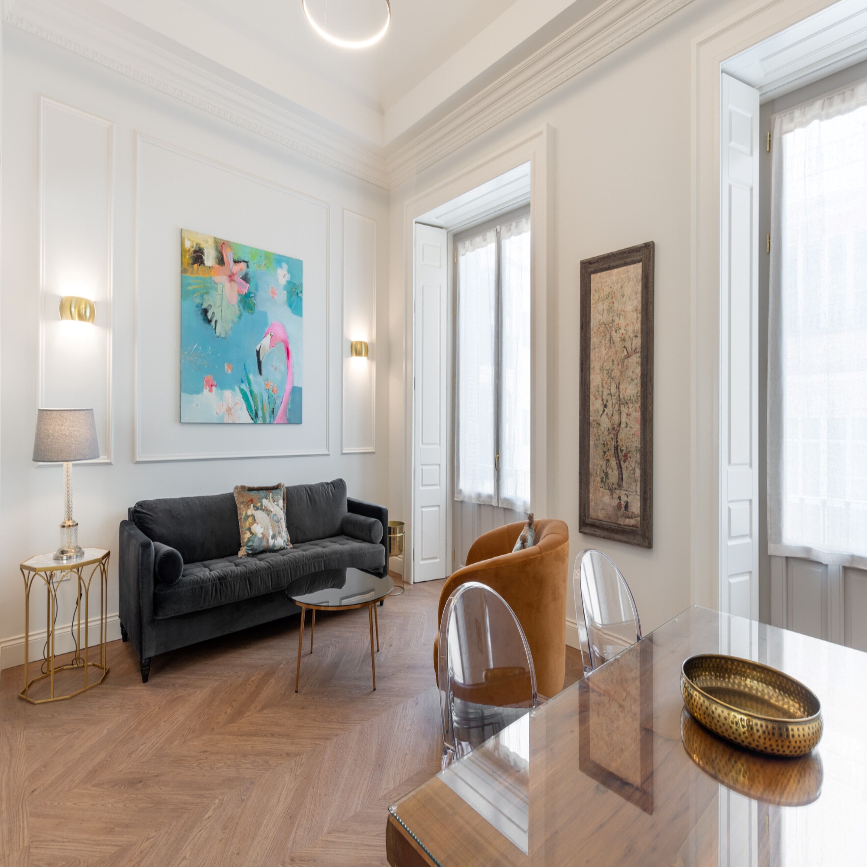 Un salón espacioso con un sofá gris oscuro, una mesa de centro redonda y un comedor con mesa y sillas de vidrio.