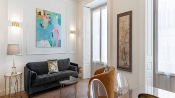 Un salón espacioso con un sofá gris oscuro, una mesa de centro redonda y un comedor con mesa y sillas de vidrio.
