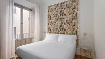 A neatly made bed with white linens, a patterned wallpaper headboard, and a small round side table with a marble top.