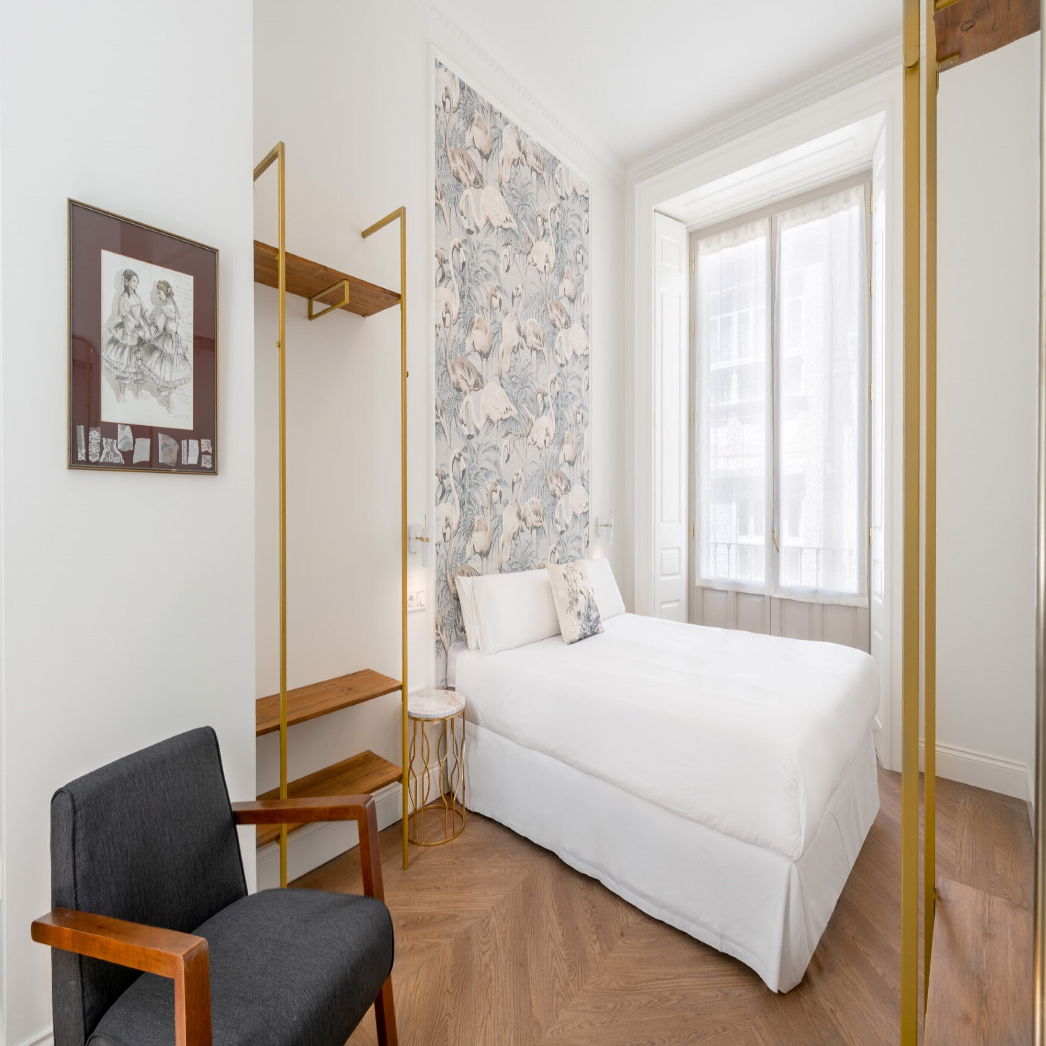 Une chambre à coucher comprenant un lit, une chaise, une petite table et un mur recouvert d’un papier peint à motifs floraux.