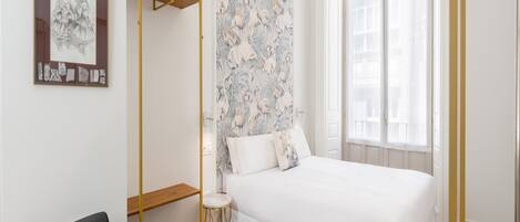 A bedroom with a bed, a chair, a small table, and a wall with floral wallpaper.