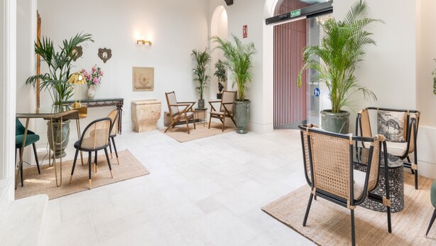 A spacious room with a high ceiling, wooden beams, a skylight, a dining area with chairs and a table, and several potted plants. - Be Mate Málaga Centro (Málaga)