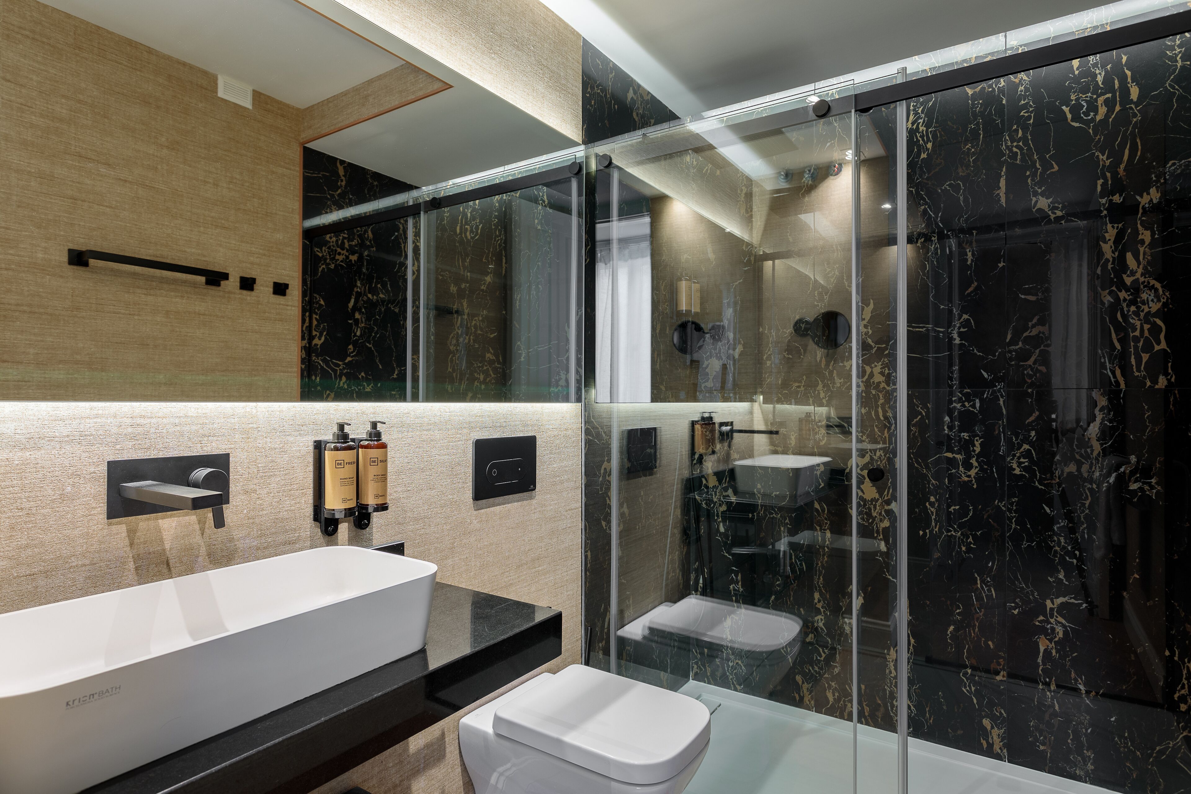 A modern bathroom with a large white sink, a glass-enclosed shower, and a marble wall.