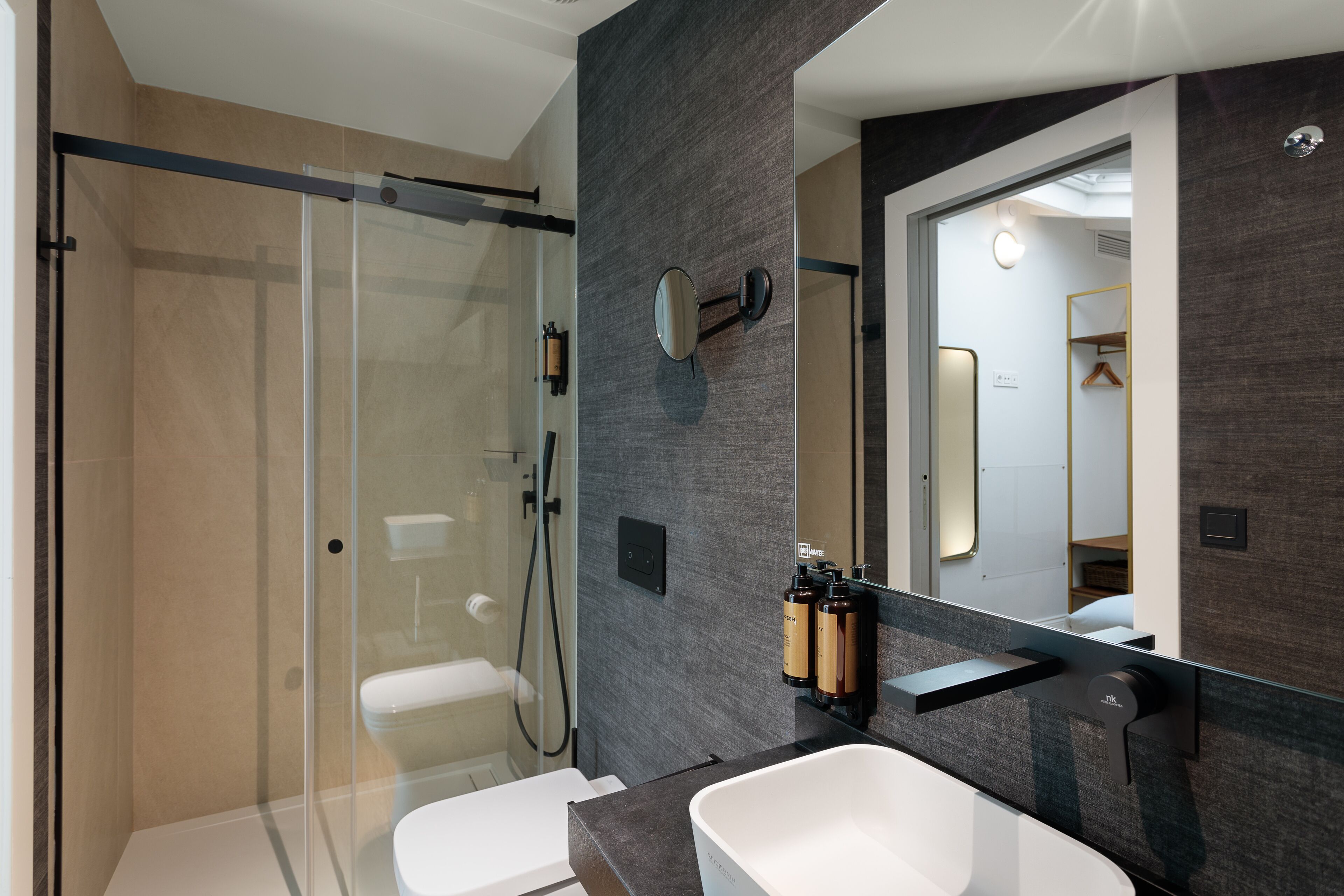 A modern bathroom with a glass-enclosed shower, a large mirror, and a white sink.