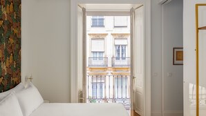 A bedroom with a large bed, a view of a balcony with buildings, and a door leading to another room. - Be Mate Málaga Centro (Málaga)