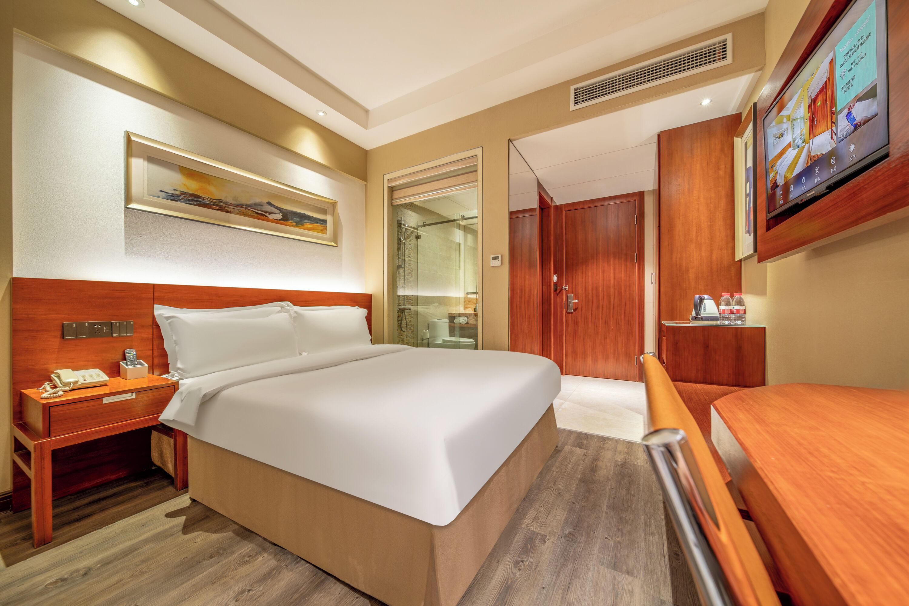 Habitación de hotel con cama, mesita de noche, televisor montado en la pared y armario de madera.