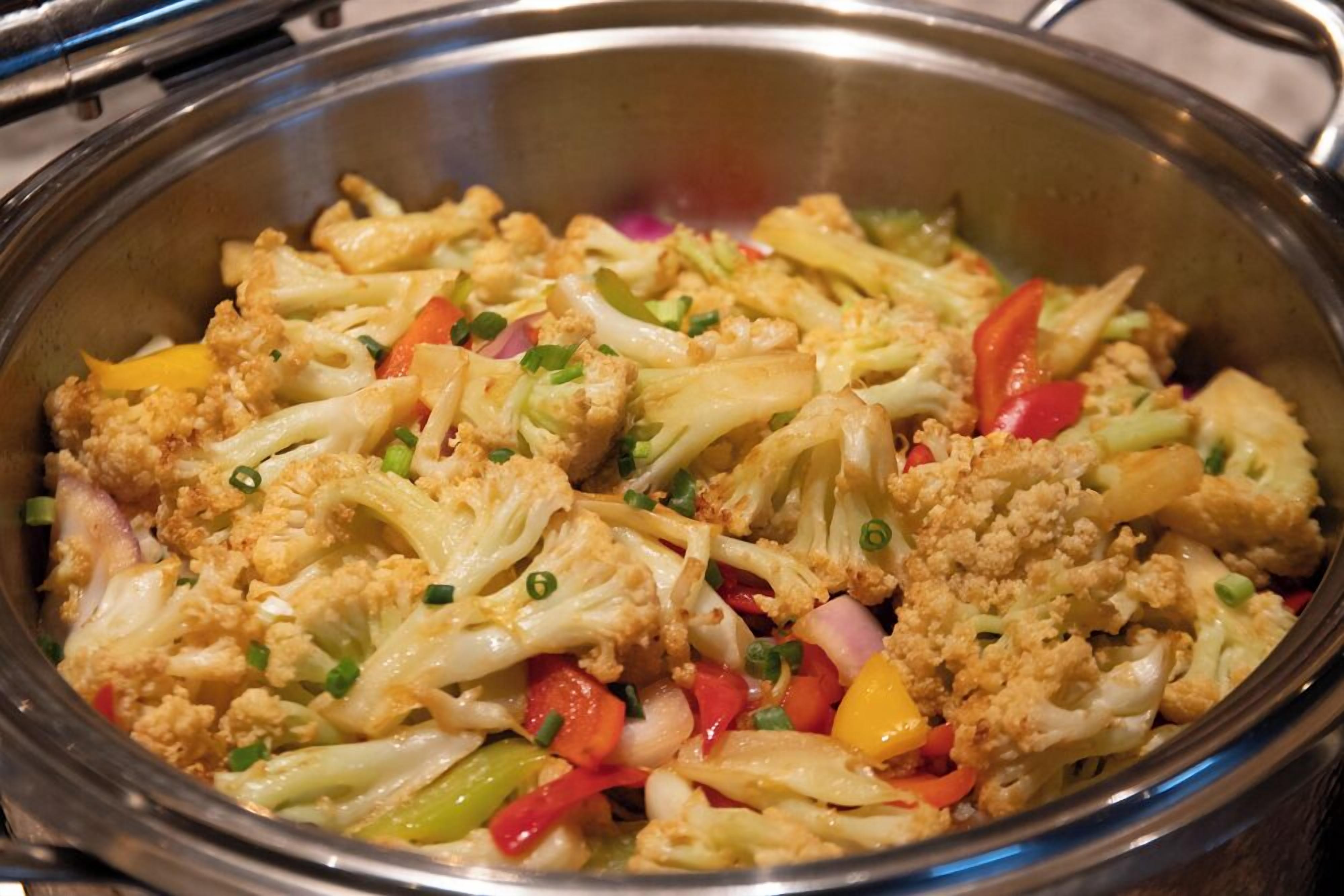 A stainless steel bowl containing a stir-fry with cauliflower, bell peppers, and onions.