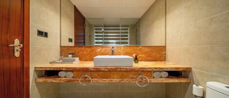 A bathroom with a marble vanity, a toilet, and a mirror.