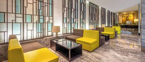 A modern lobby with yellow seating, a reception desk, and a decorative wall.