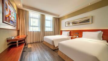 A hotel room with two beds, a desk, a chair, a TV, and a painting on the wall.