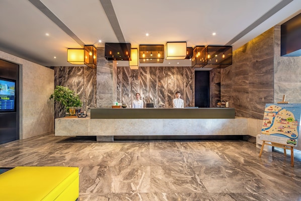 A reception area with a marble wall, a reception desk, two staff members, a digital screen, and a yellow seating area. - Maixinge Boutique Hotel (Shanghai)