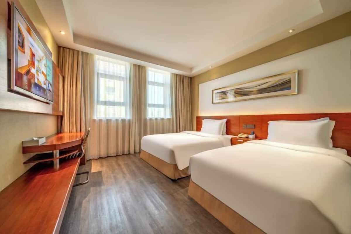 A hotel room with two beds, a desk, and a painting on the wall.