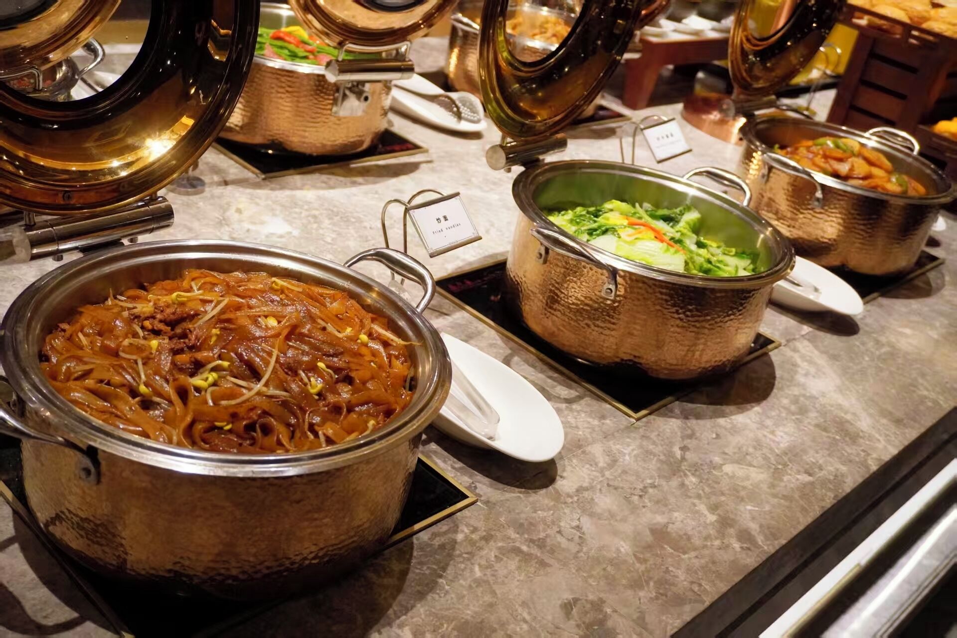 A buffet with various dishes, including noodles and a pot of soup.