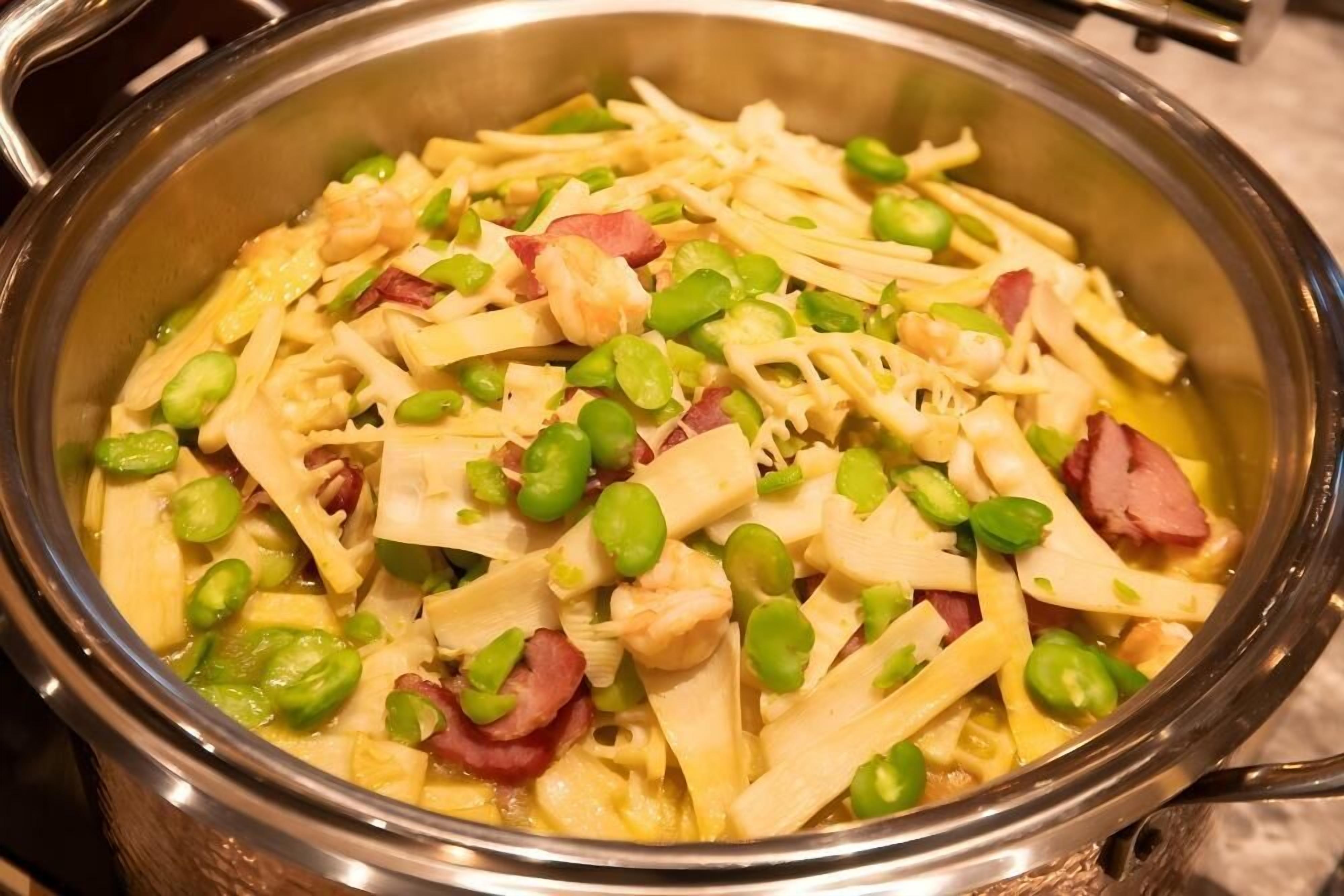 Una olla de acero inoxidable llena de pasta, guisantes verdes y trozos de jamón.