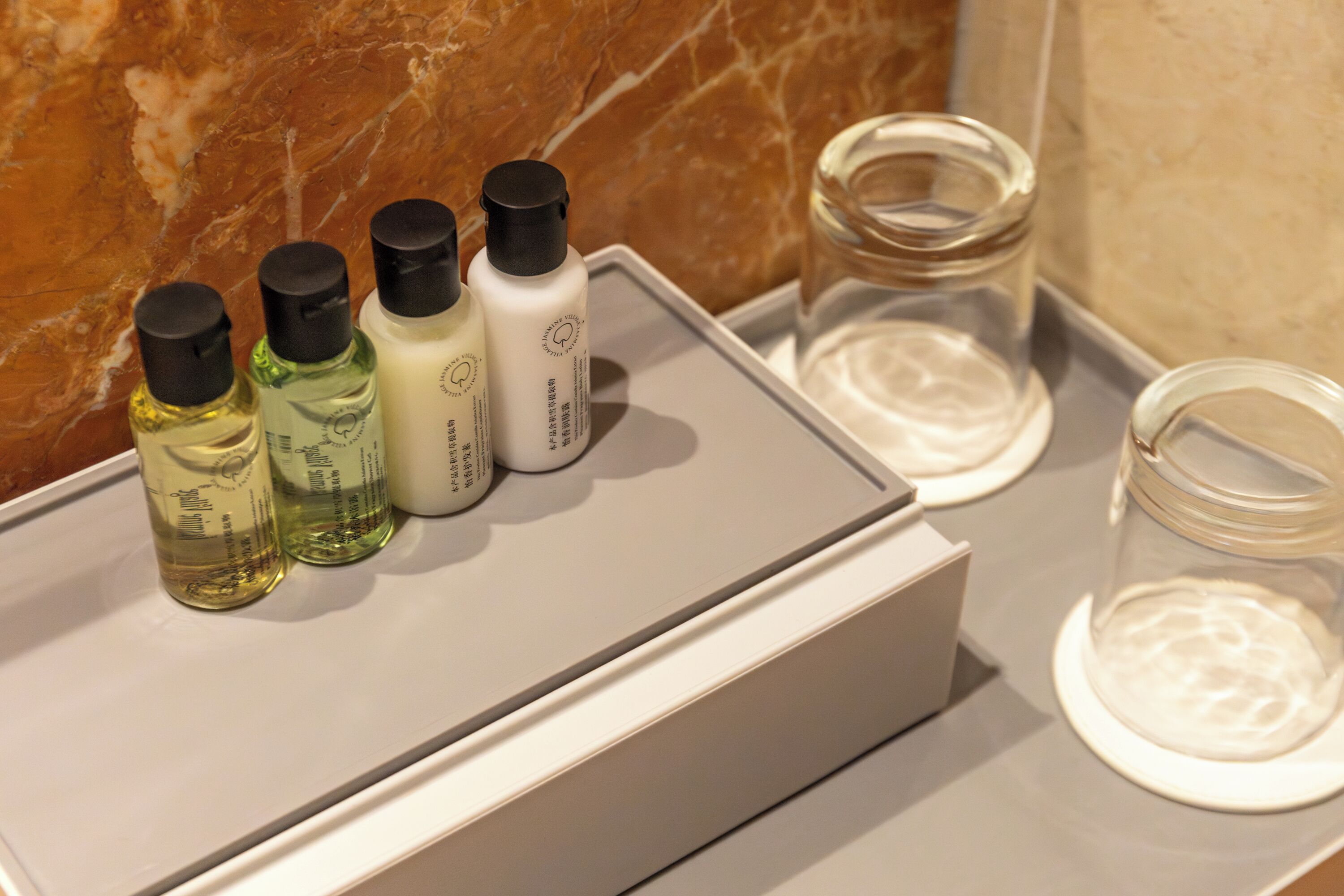 Un tocador de baño con encimera de mármol, una caja blanca con artículos de aseo y un frasco de vidrio.