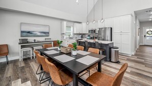 A modern kitchen with white cabinets, a stainless steel refrigerator, and a dining area with a black table and brown chairs. - Indoor/Outdoor Pool, Pickleball, Private Hot tub (Hollister)