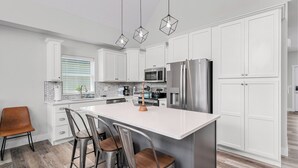 A modern kitchen with white cabinets, stainless steel appliances, and a central island with bar stools. - Indoor/Outdoor Pool, Pickleball, Private Hot tub (Hollister)