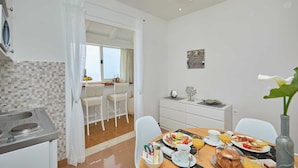 A modern kitchen with a dining area, featuring a breakfast setup with plates of food, a coffee cup, and a vase with a flower.