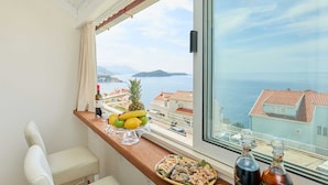 A balcony with a table set with fruits, a bottle of wine, and a view of the sea.