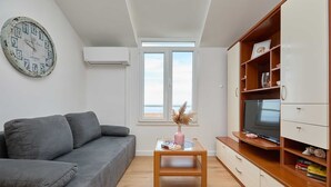 A modern living room with a grey sofa, a wooden coffee table, a TV on a wooden stand, and a bookshelf.