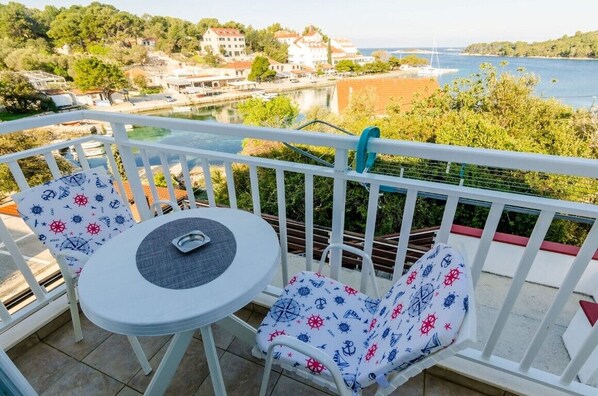 En balkon med et bord og stole, udsigt over vand og bygninger.
