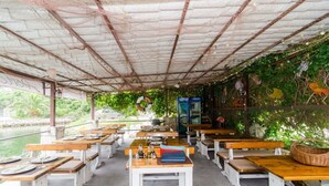 Un área de comedor al aire libre con mesas y bancos de madera, techo cubierto y vista a un cuerpo de agua.